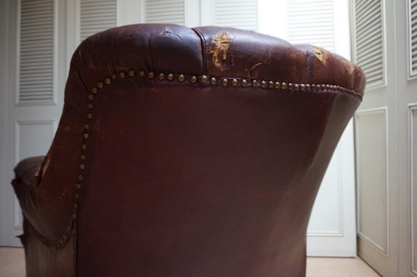 Achter aanzicht van een antieke Edwardiaanse herenfauteuil op wieltjes als restauratieproject